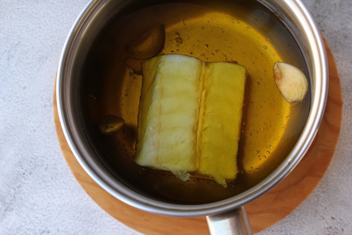 lomo de bacalao sumergido en aceite de oliva virgen extra para ser confitado a baja temperatura *